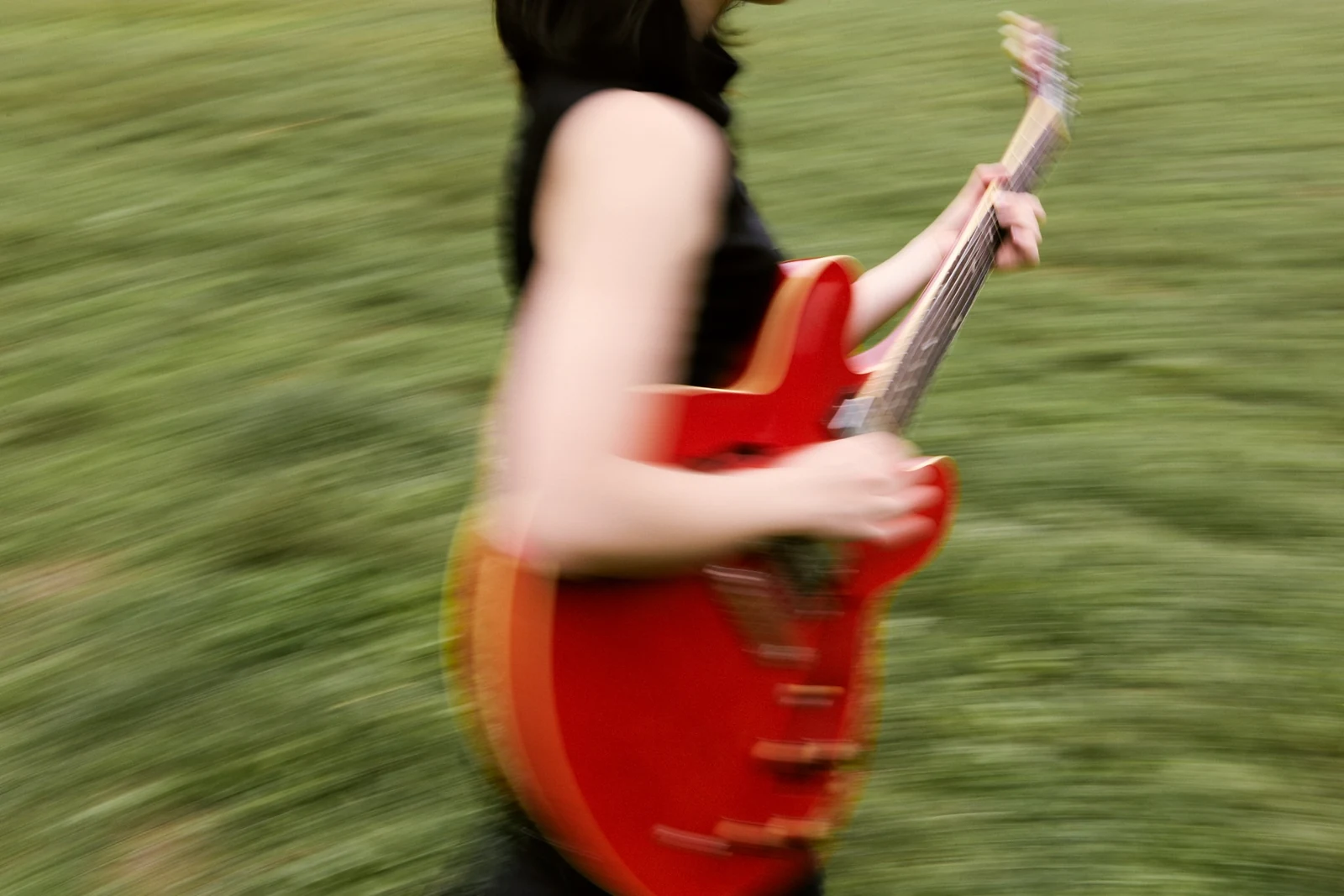 Erika Toda holding a red electric guitar in a motion-blurred outdoor photograph
